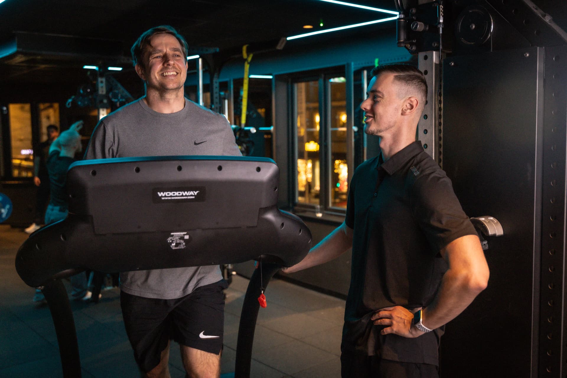 Mann løper på Woodway-tredemølle mens en Torp&Co-trener følger med og smiler i treningsstudioet.
