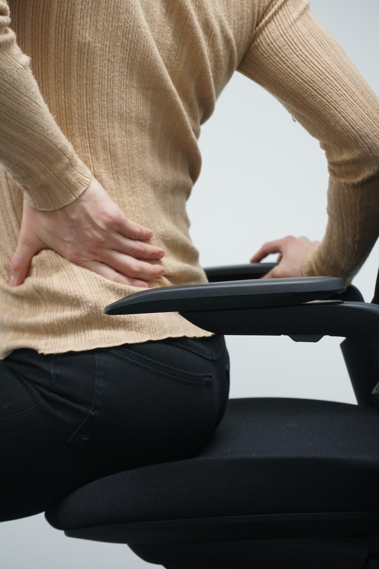 Person holder seg i korsryggen mens de sitter i en kontorstol