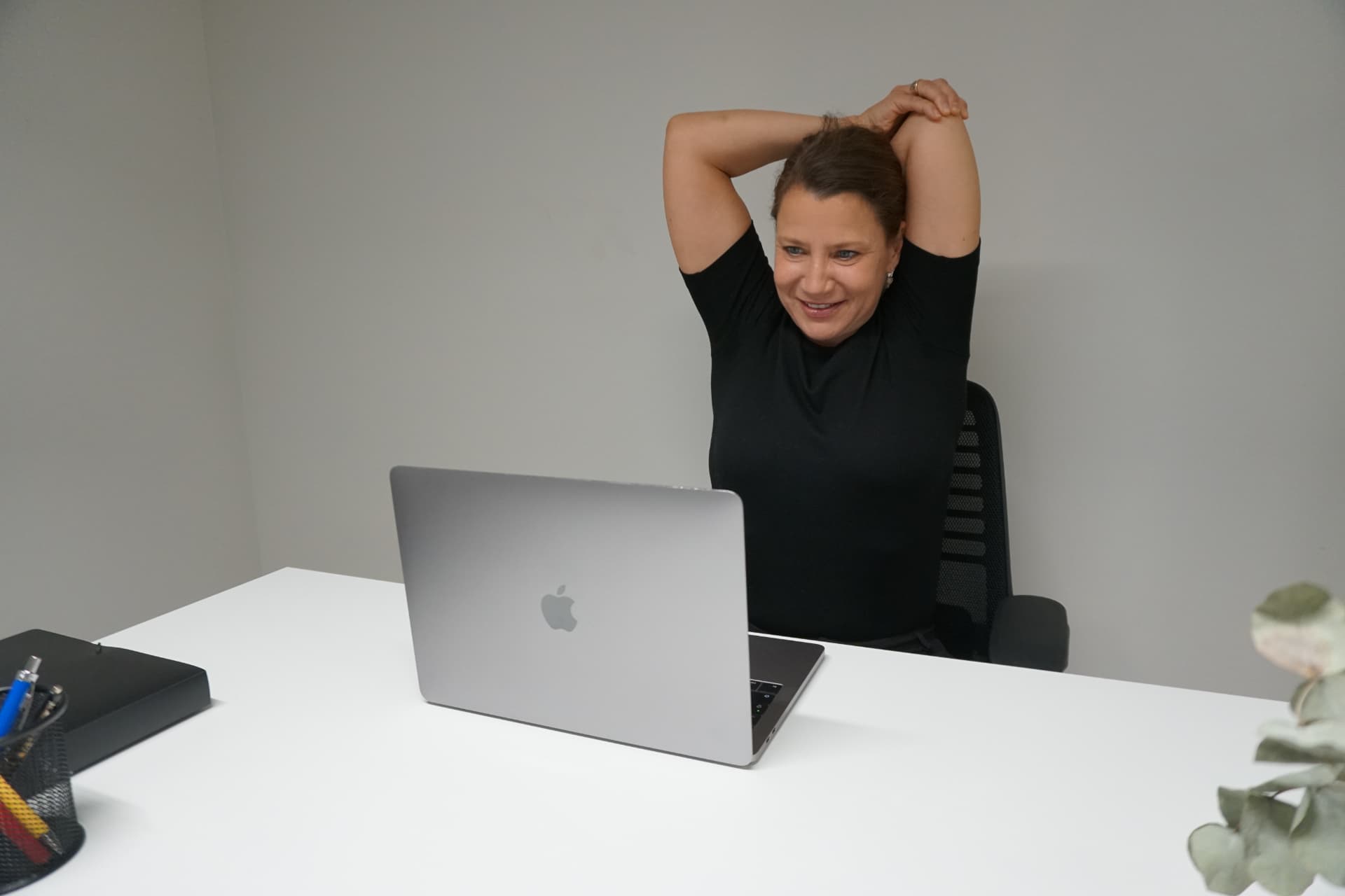 Kvinne strekker armer bak hodet ved ergonomisk hjemmekontor — tips fra fysioterapeut